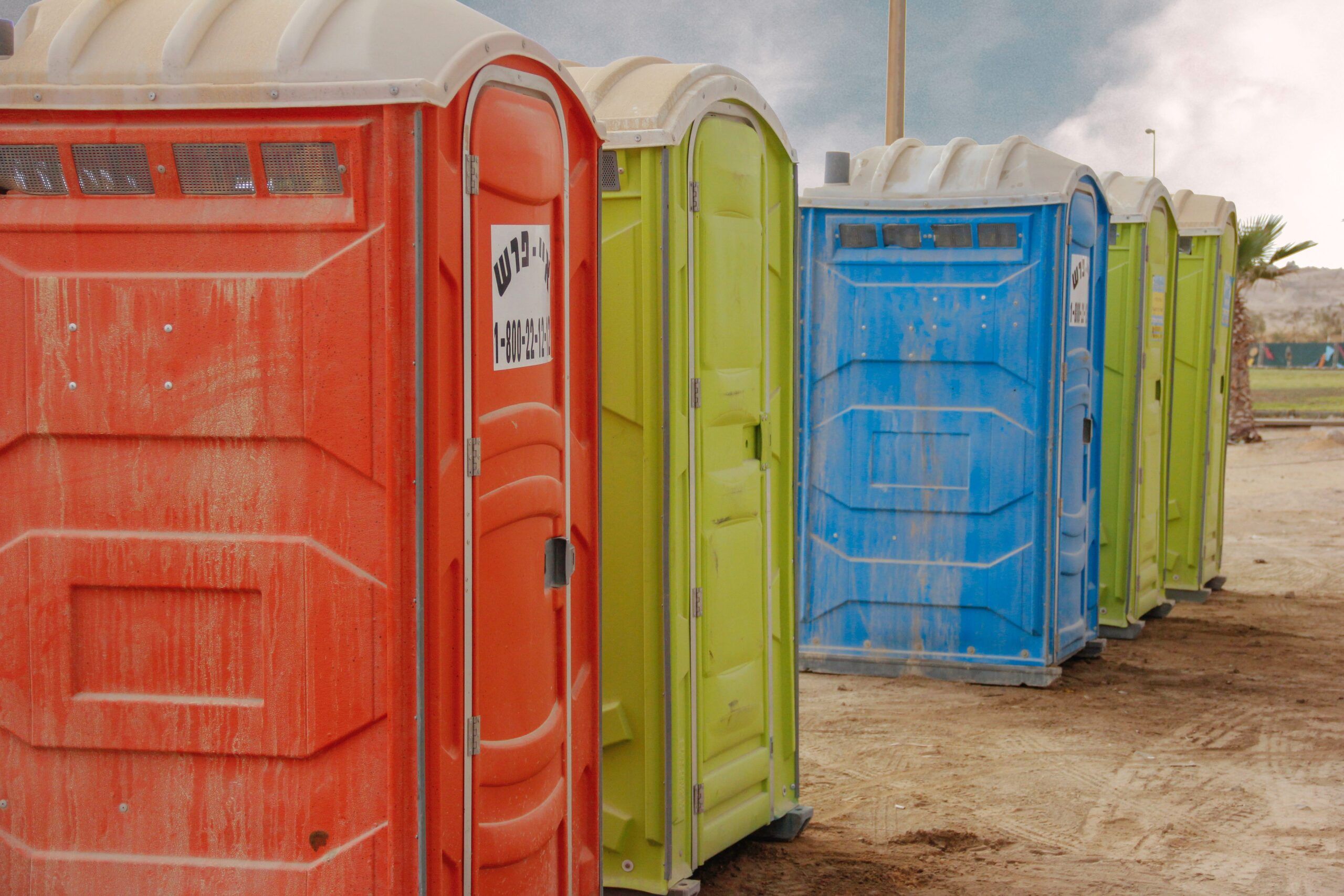 Row of red, yellow and blue portable toilets on sand